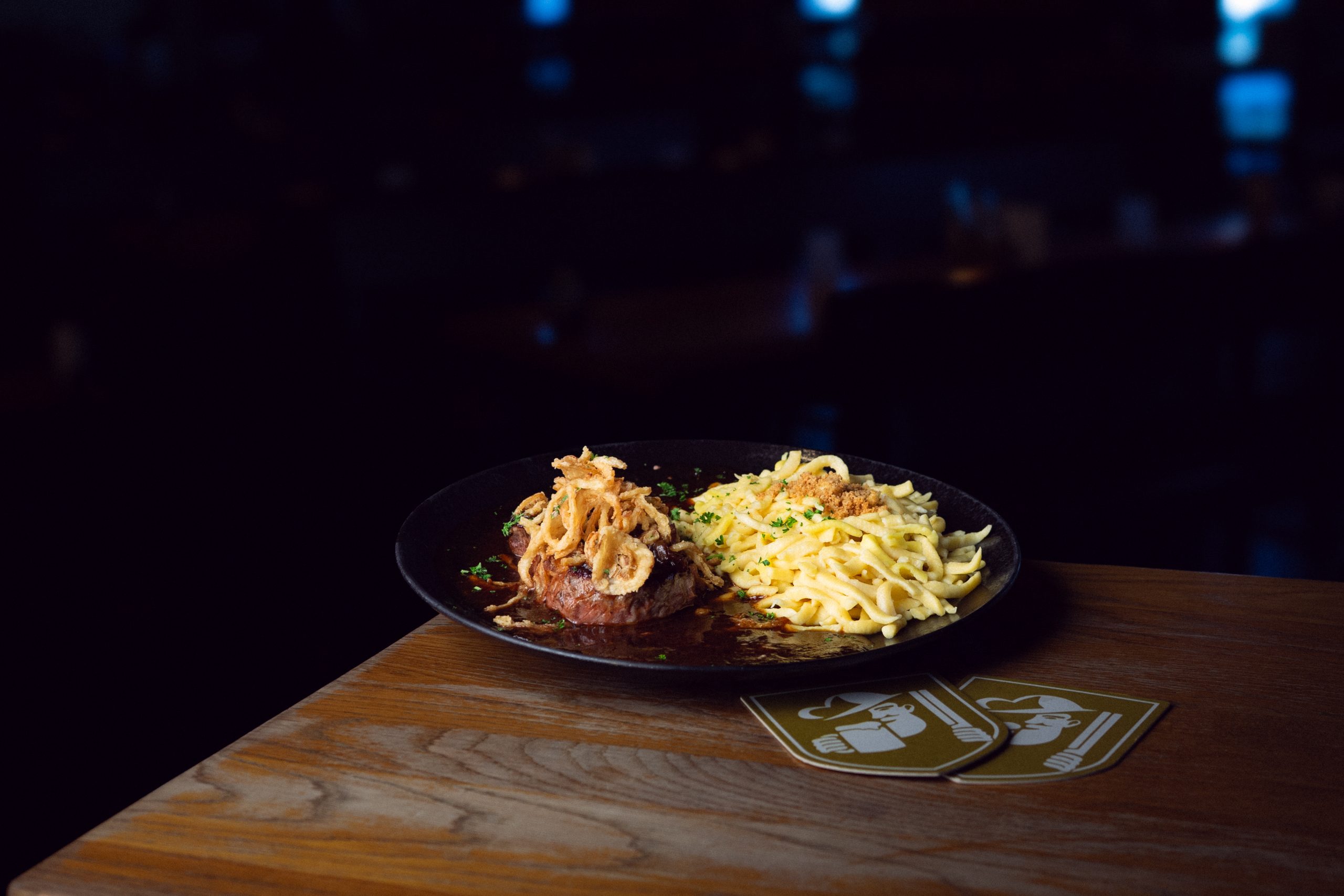 Spätzle mit Sauce und einem Stück Fleisch auf einem schwarzen Teller im Brauhaus.