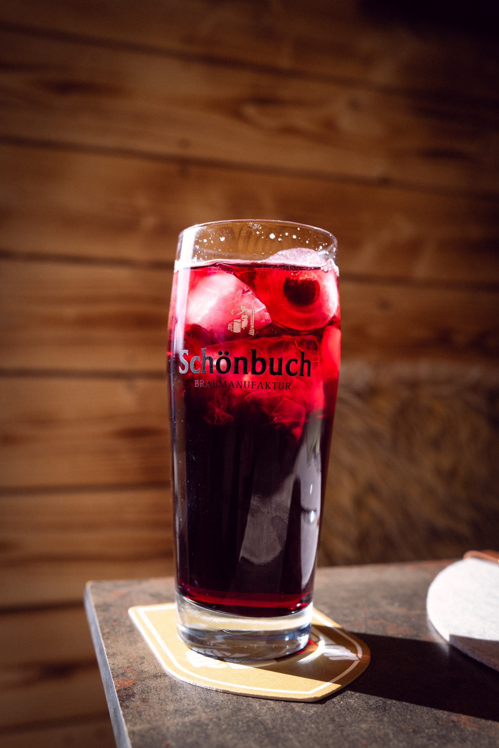 Rotes Getränk im Glas mit Eis und Früchten auf Holztisch im Brauhaus Schönbuch.