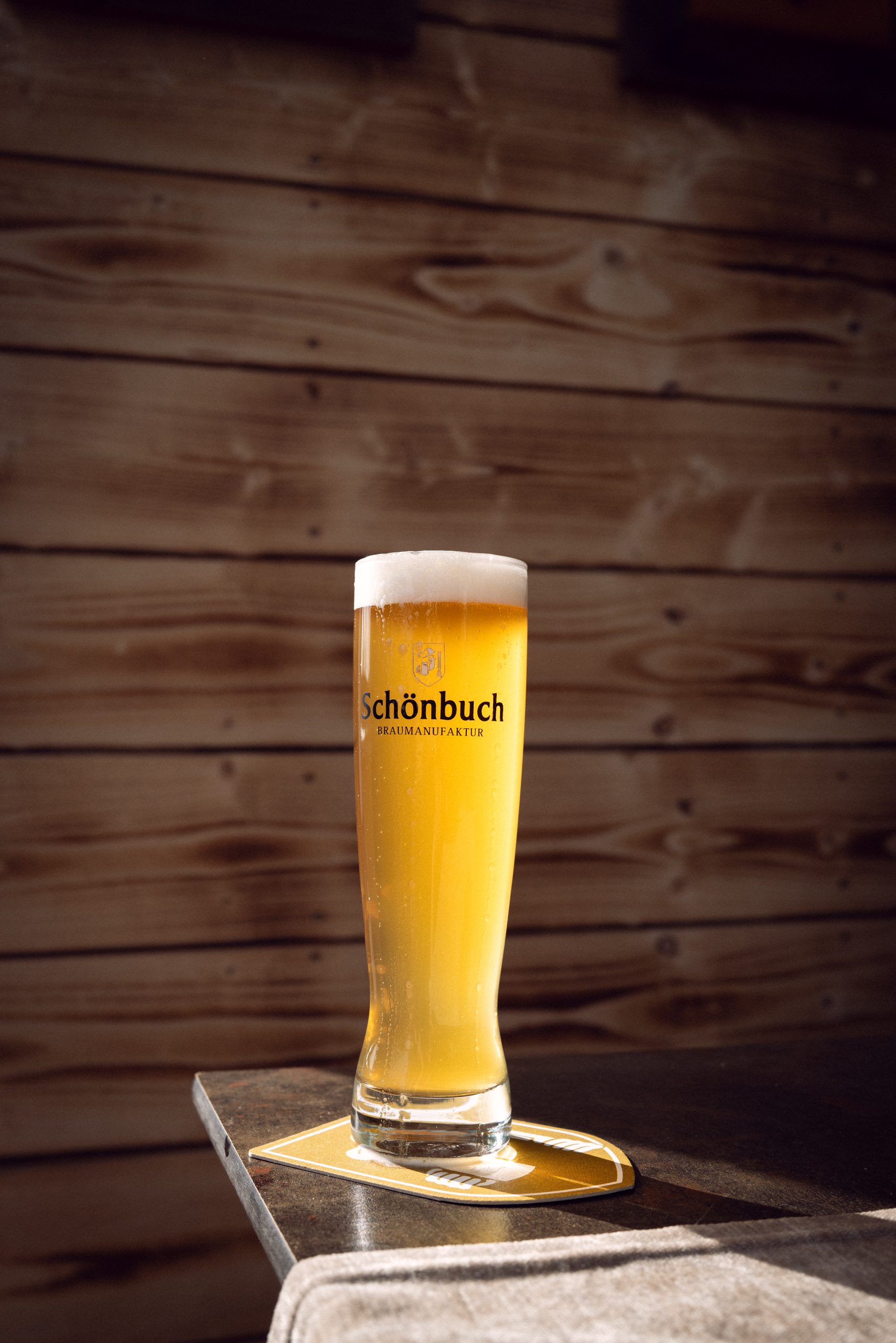 Frisch gezapftes helles Bier im Glas mit Schönbuch-Logo vor Holz-Hintergrund.