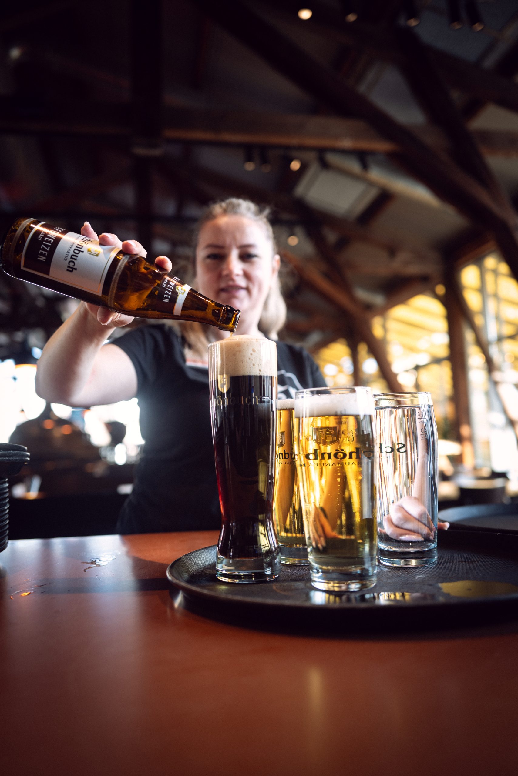 Servicekraft schenkt dunkles Bier aus einer Flasche in ein Glas ein.